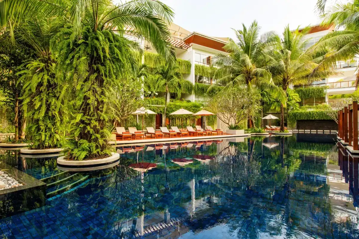 Outdoor swimming pool surrounded by tropical palm trees and sun loungers at The Chava Resort Phuket.