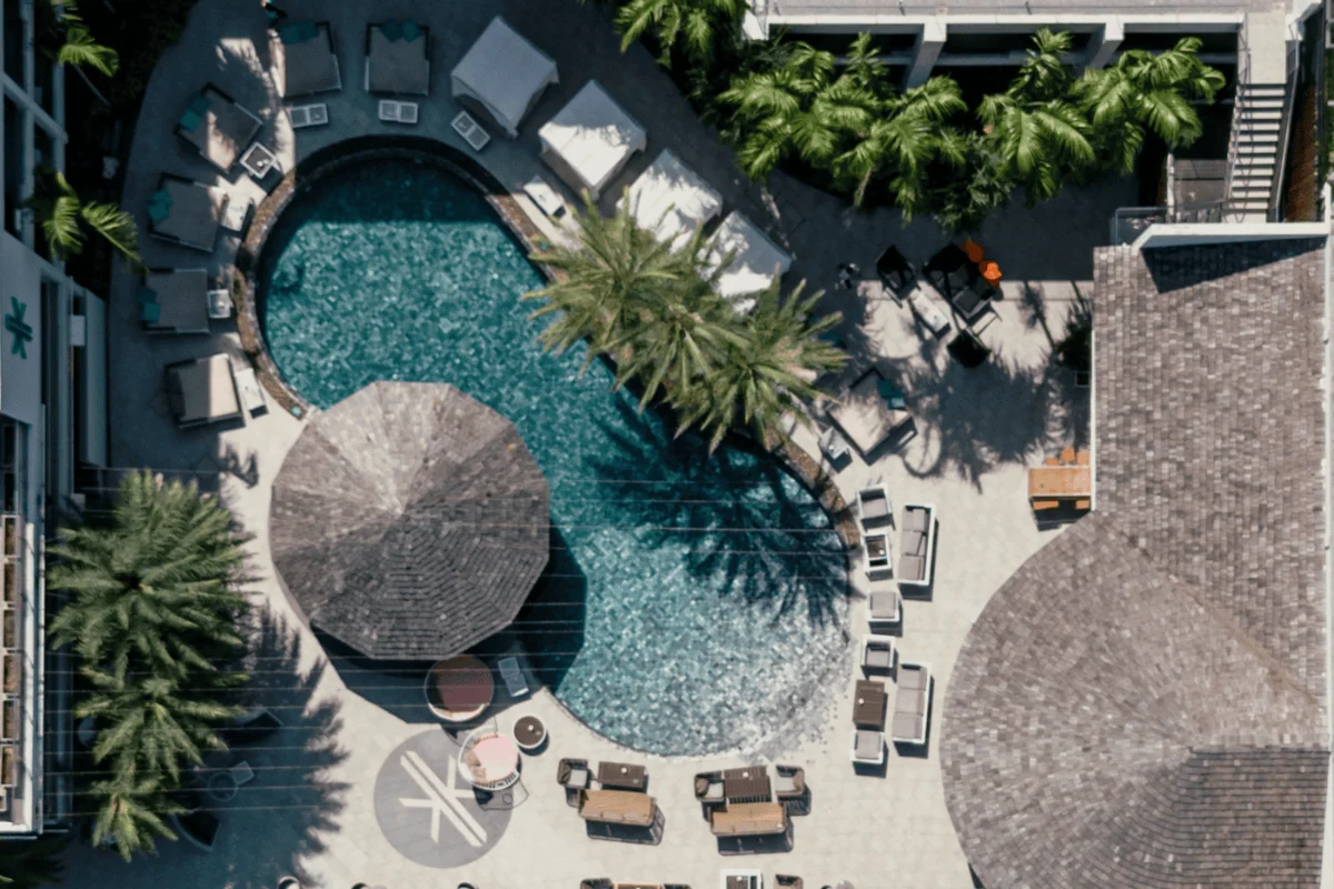 Aerial top-down view of the outdoor swimming pool, sun loungers, and tropical palm trees at Kudo Hotel & Beach Club Patong.