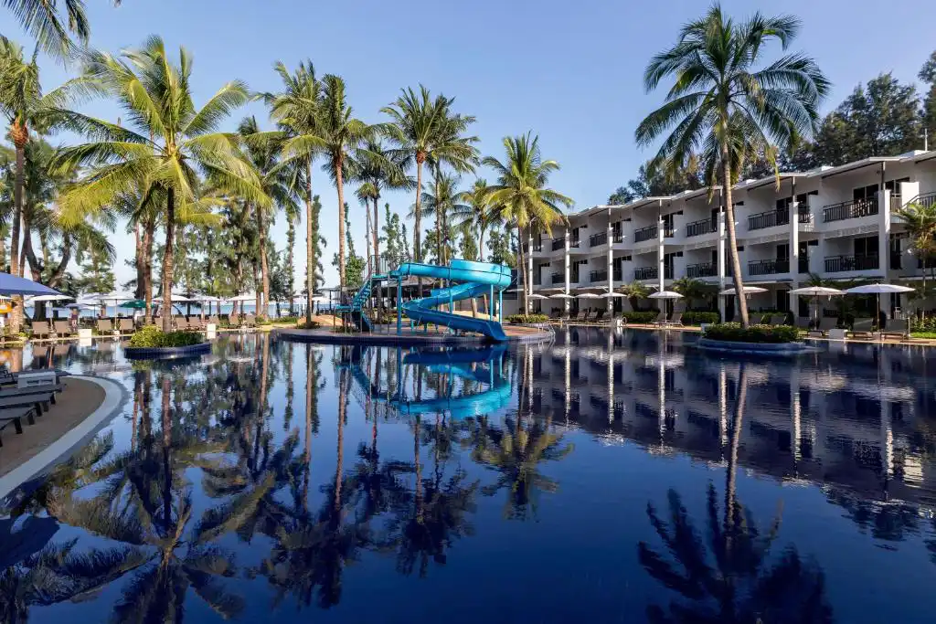 Outdoor swimming pool with a blue water slide, palm trees, and guest room buildings at Sunwing Bangtao Beach Resort Phuket.