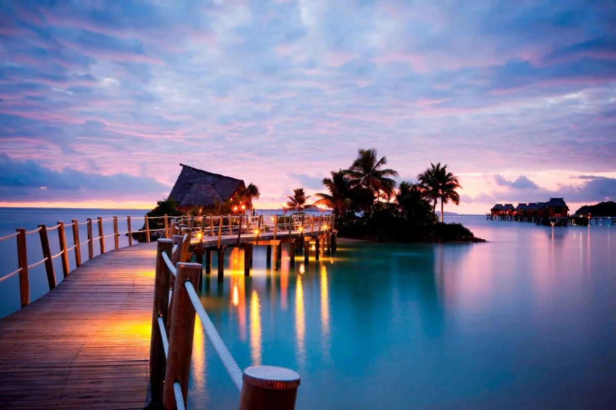 Boardwalk leading to overwater bures and lagoon views at Likuliku Lagoon Resort Fiji during sunset.