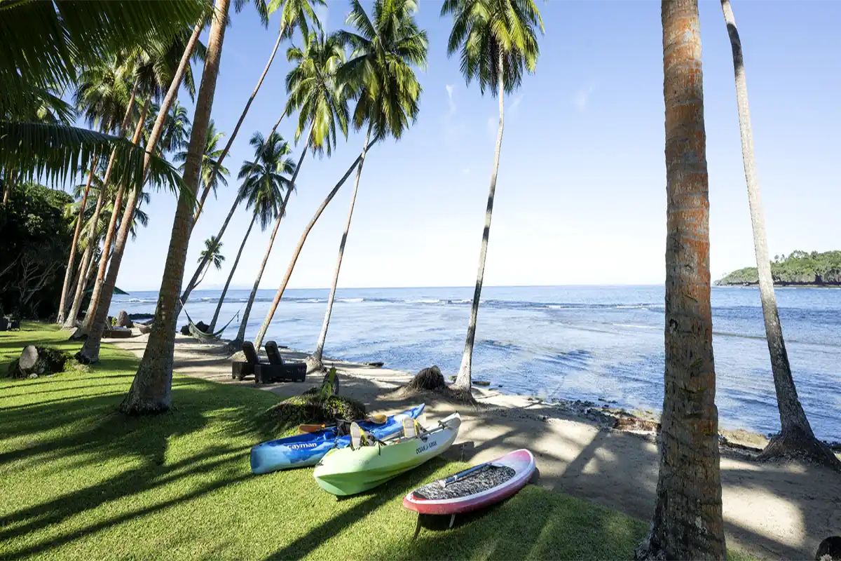 Ocean kayaks and stand-up paddleboards lined up on the beachfront lawn at Namale Resort & Spa in Fiji.