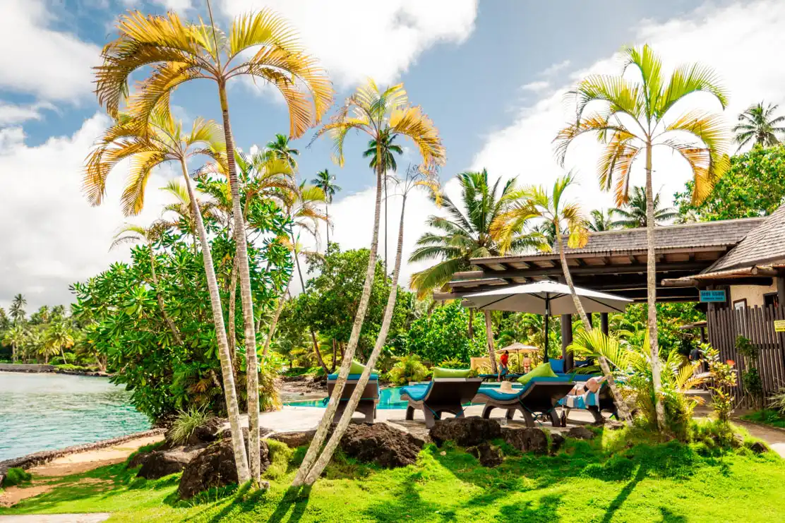 Outdoor swimming pool and lounge chairs surrounded by palm trees at Koro Sun Resort & Rainforest Spa in Fiji.