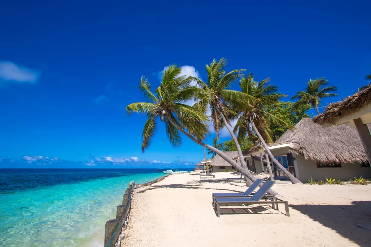 Ocean Front Bure view and sun loungers on white sand beach at Castaway Island Fiji resort in Mamanuca Islands.