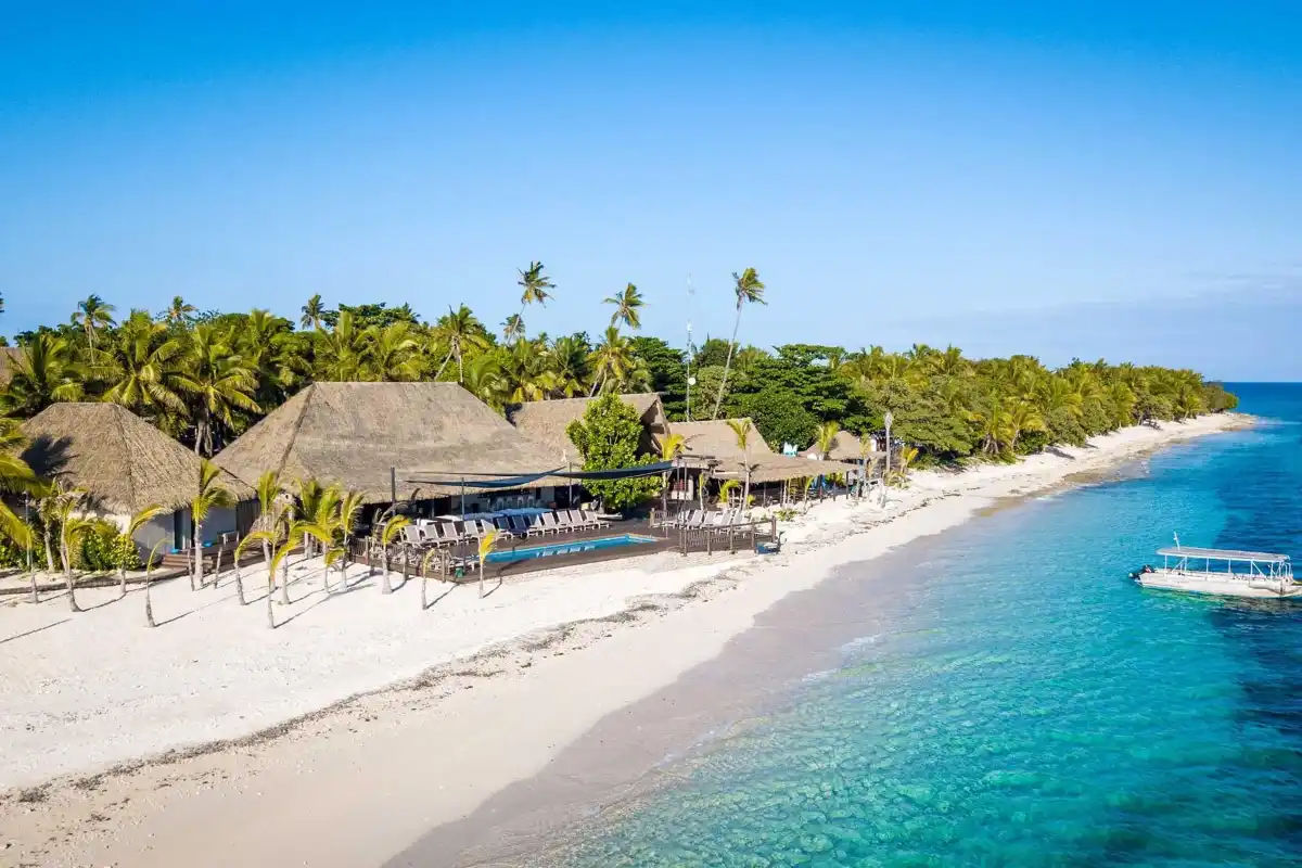 Aerial view of Serenity Island Resort Fiji featuring the beachfront swimming pool, white sand shore, and thatched-roof bures.