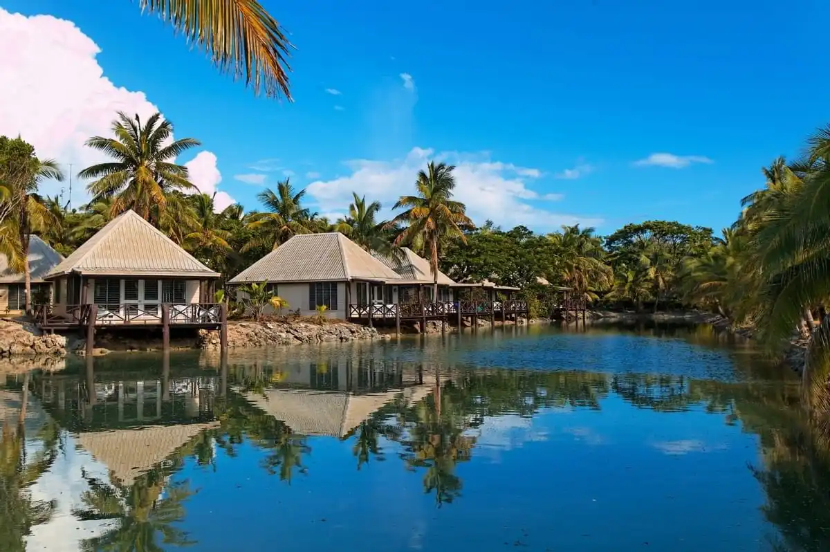 Lagoonfront bures with wooden balconies surrounded by palm trees at Musket Cove Island Resort Fiji.
