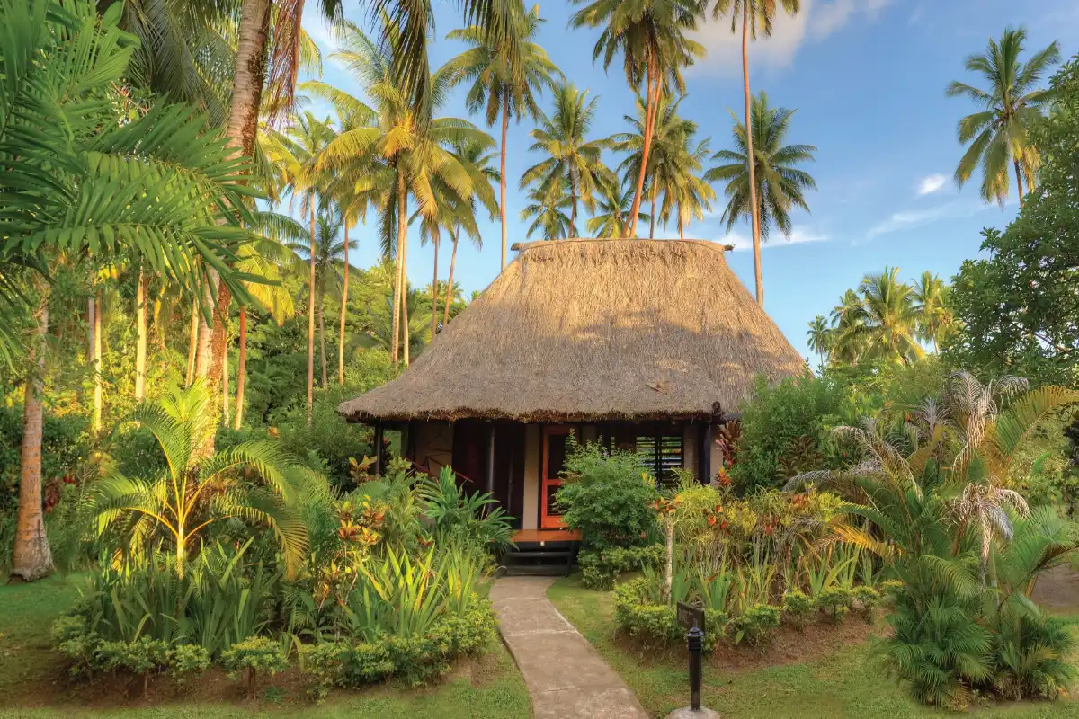 Traditional thatched-roof Garden View Bure villa surrounded by palm trees at Jean-Michel Cousteau Resort Fiji.