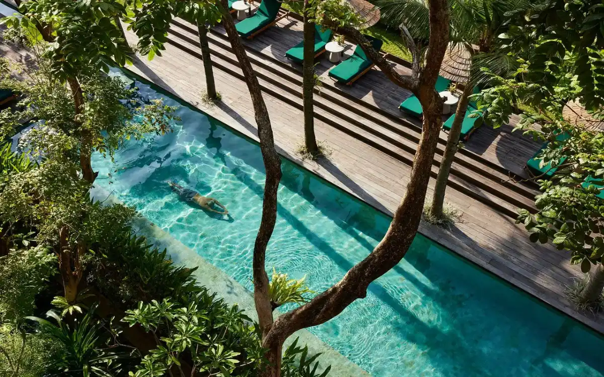 Outdoor swimming pool with wooden sun deck and green loungers at Desa Potato Head Bali Seminyak
