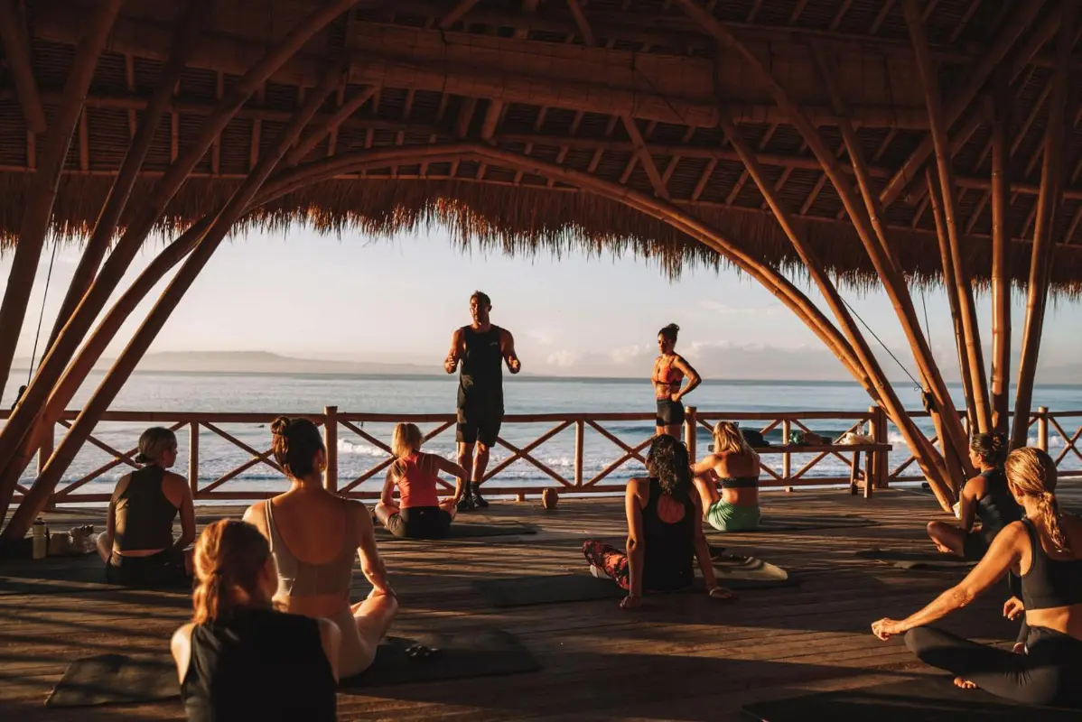 Group fitness and yoga session inside the open-air bamboo shala at Hotel Komune and Beach Club Bali facing Keramas Beach