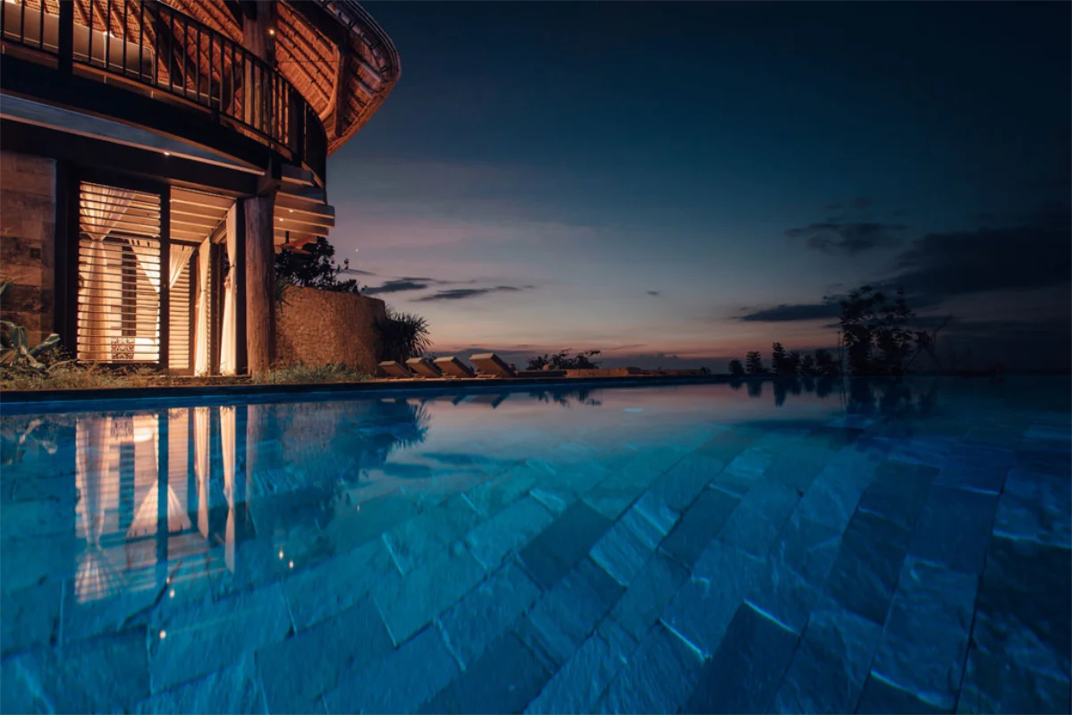 Illuminated infinity pool and bamboo villa architecture at Suarga Padang Padang Uluwatu during twilight