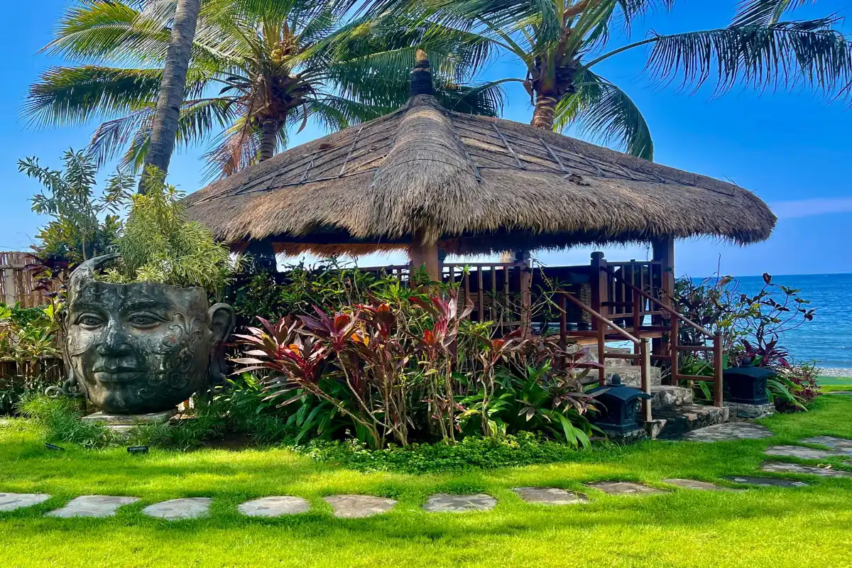 Beachfront wooden gazebo and stone sculpture in the tropical garden at Louka Beach Bali Tianyar