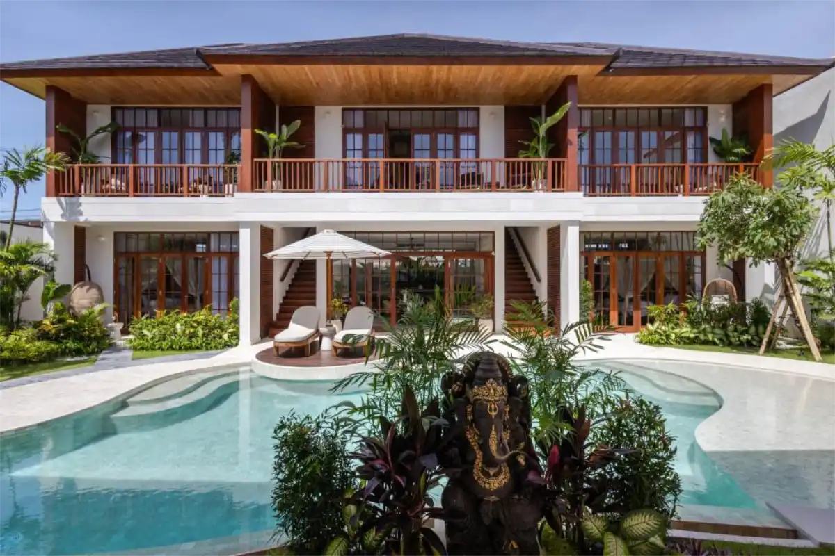 Exterior view from the poolside of Plawa Laguna, a two-story luxury rental villa with a tropical garden, private pool, and a Ganesha statue in Pererenan, Bali.