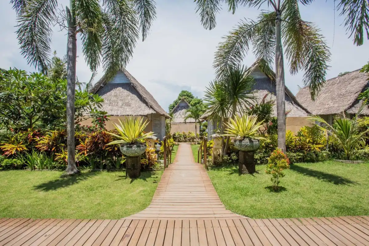 Traditional wooden bungalows aligned along a garden pathway surrounded by palm trees at Bay Shore Huts Nusa Lembongan.