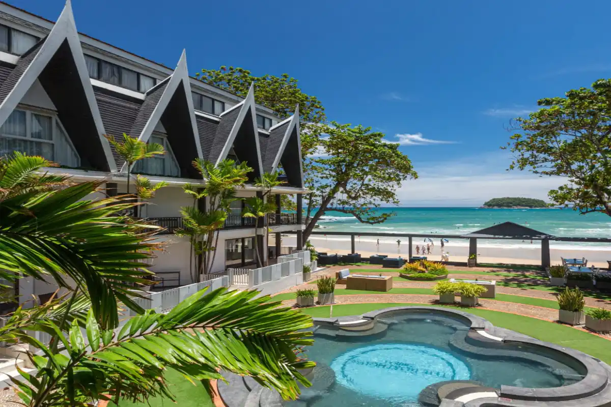 Exterior view of The Boathouse Phuket hotel featuring ocean-view balconies, an outdoor pool, and Kata Beach.