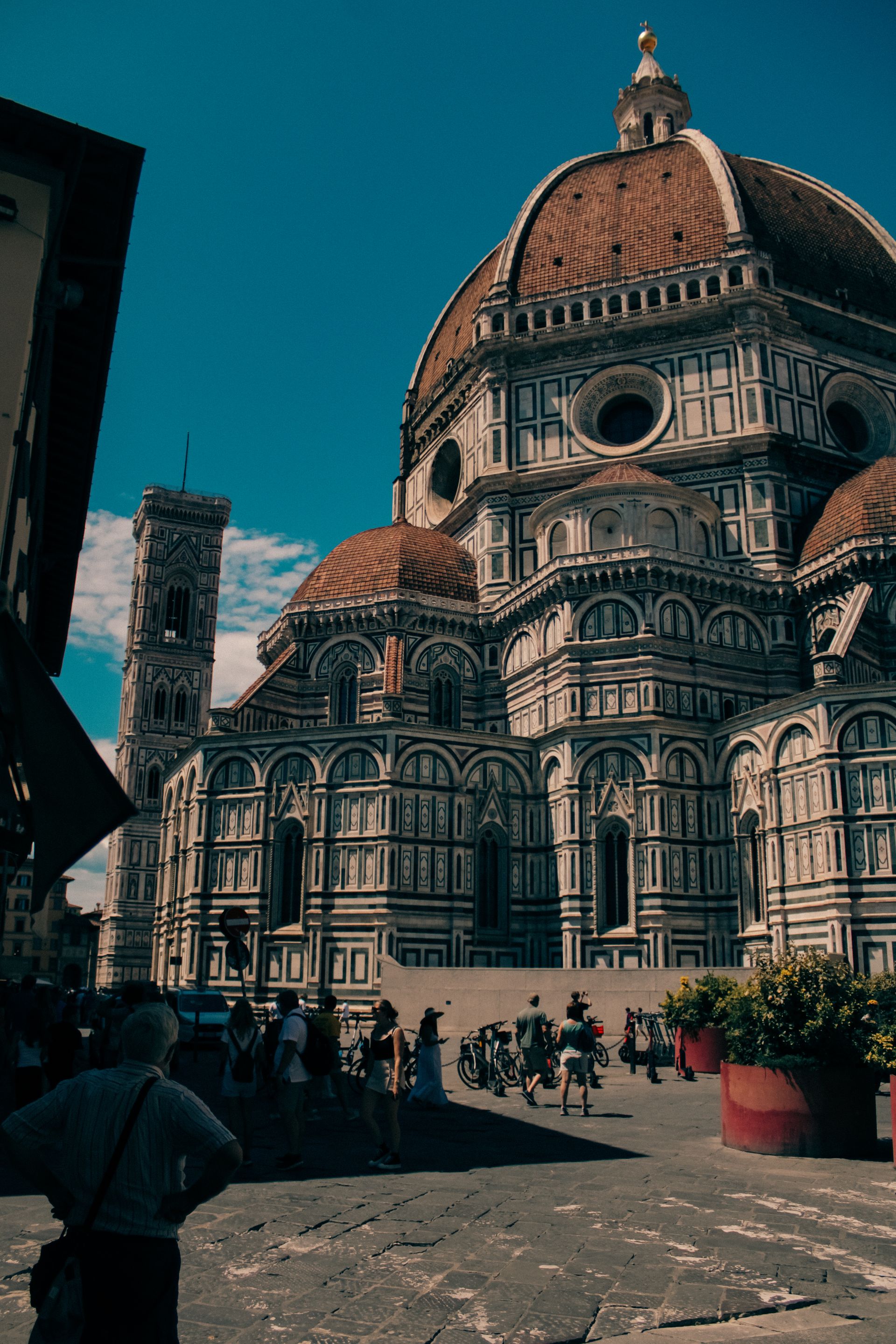 The massive red dome and white-green marble facade of the Florence Duomo Cathedral, with Giotto's Bell Tower rising in the background on a sunny day.