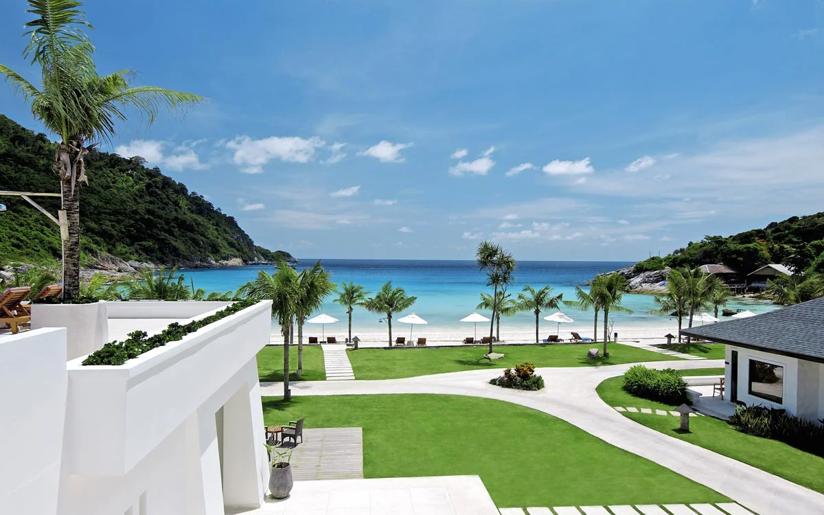 White beachfront villas, palm garden, and direct coast access at The Racha Phuket in Batok Bay.