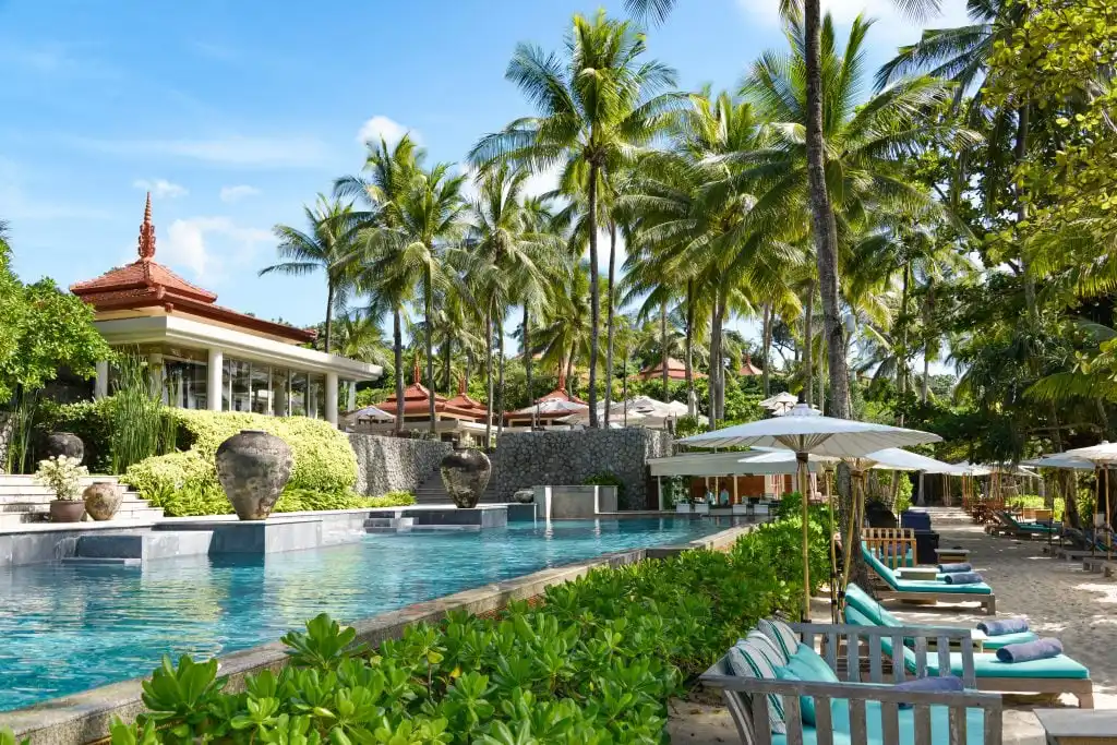 Main outdoor swimming pool and sun loungers surrounded by palm trees at Trisara Villas Phuket