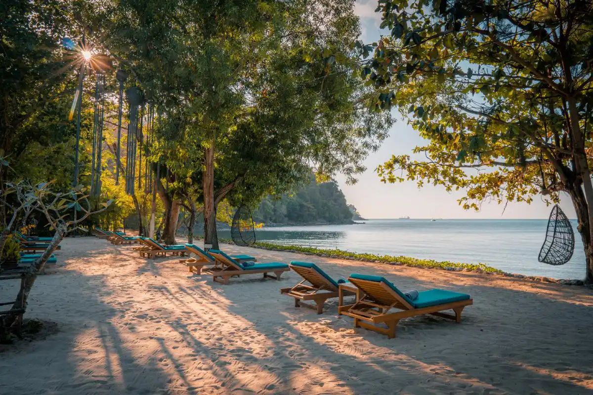 Wooden sun loungers lined under shade trees on the beach at The Mooring Resort overlooking Ao Yon Bay.