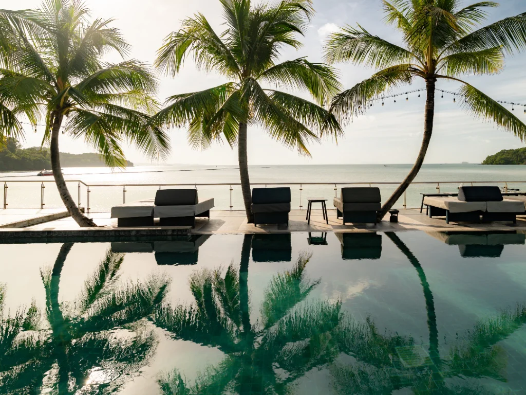 Outdoor swimming pool at Hotel Tide Phuket Beach Front with sun loungers, palm trees, and ocean views.