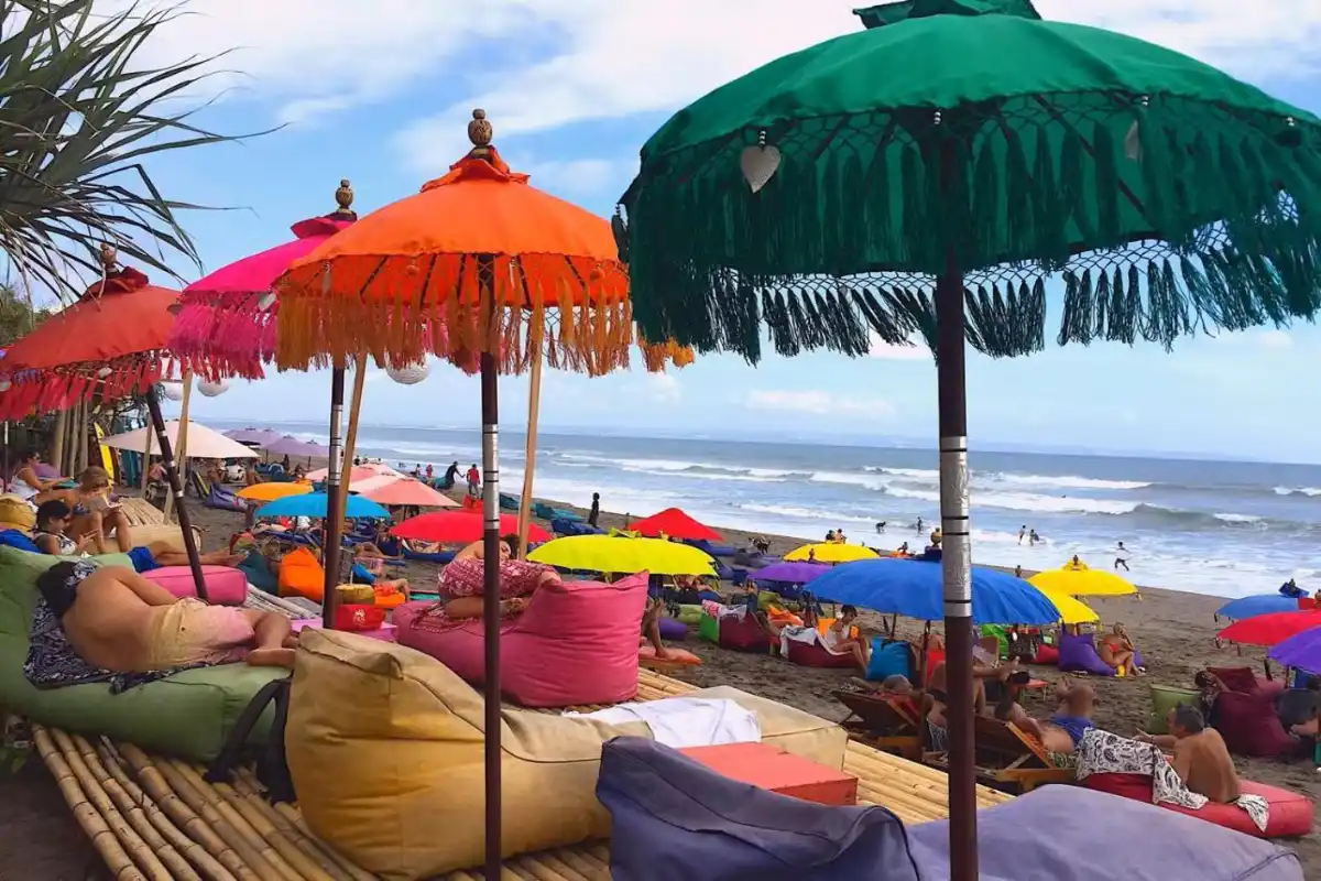 Active travelers relax under colorful umbrellas on a vibrant Canggu beach in Bali, near the AmantraNa hotel. The property offers a strategic location just minutes from popular yoga and fitness studios like The Canggu Studio and Ubud Bali Eco Yoga Retreat.