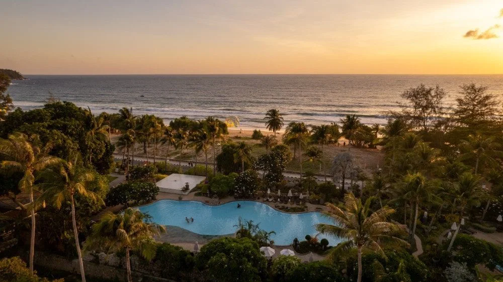 Aerial sunset view of the outdoor swimming pool, palm gardens, and Karon Beach road at Thavorn Palm Beach Resort Phuket.
