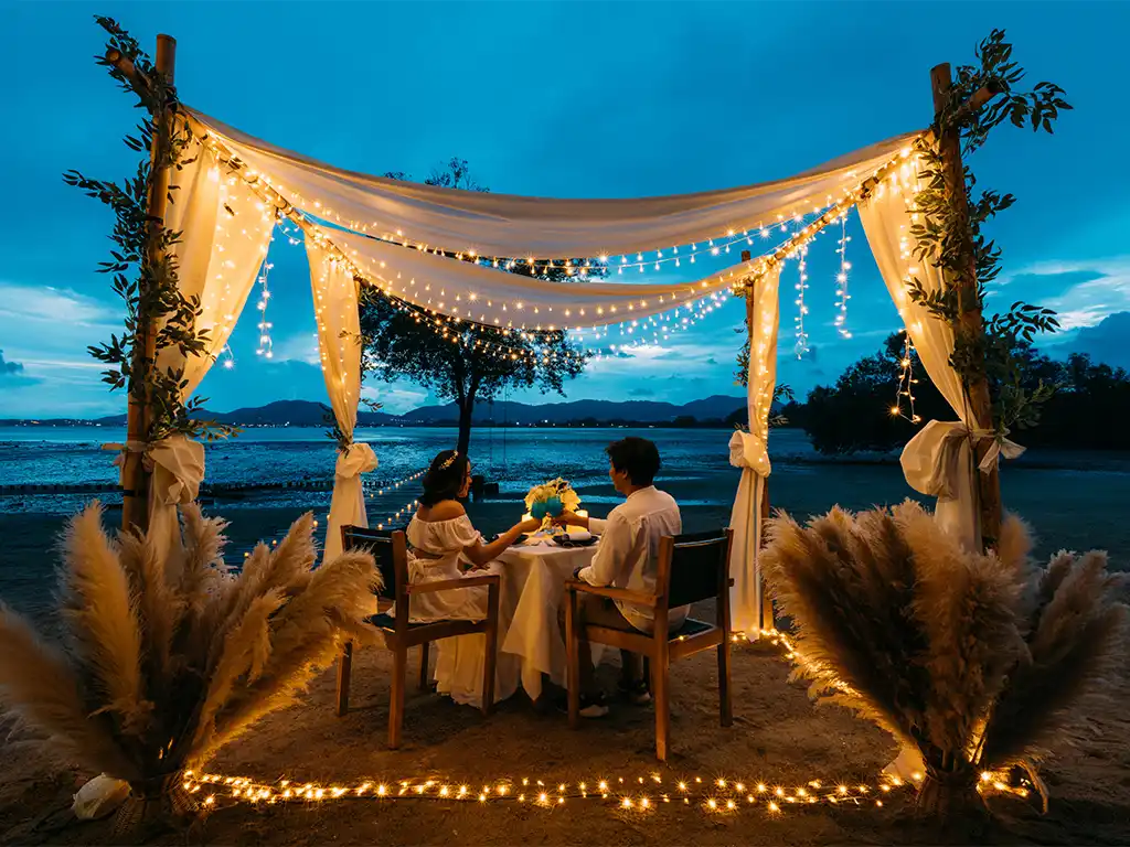 Couple dining inside an illuminated bamboo gazebo on the beach at The Mangrove by Blu Monkey Phuket.